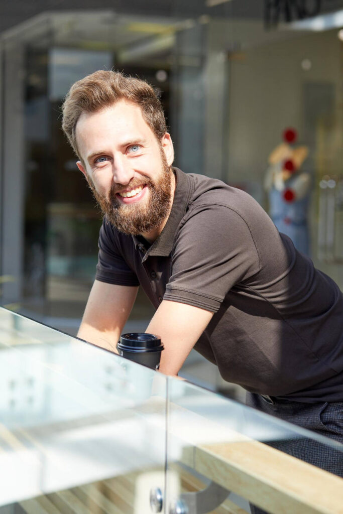 Ein Mann mit Bart und Uhr posiert in einem Einkaufszentrum