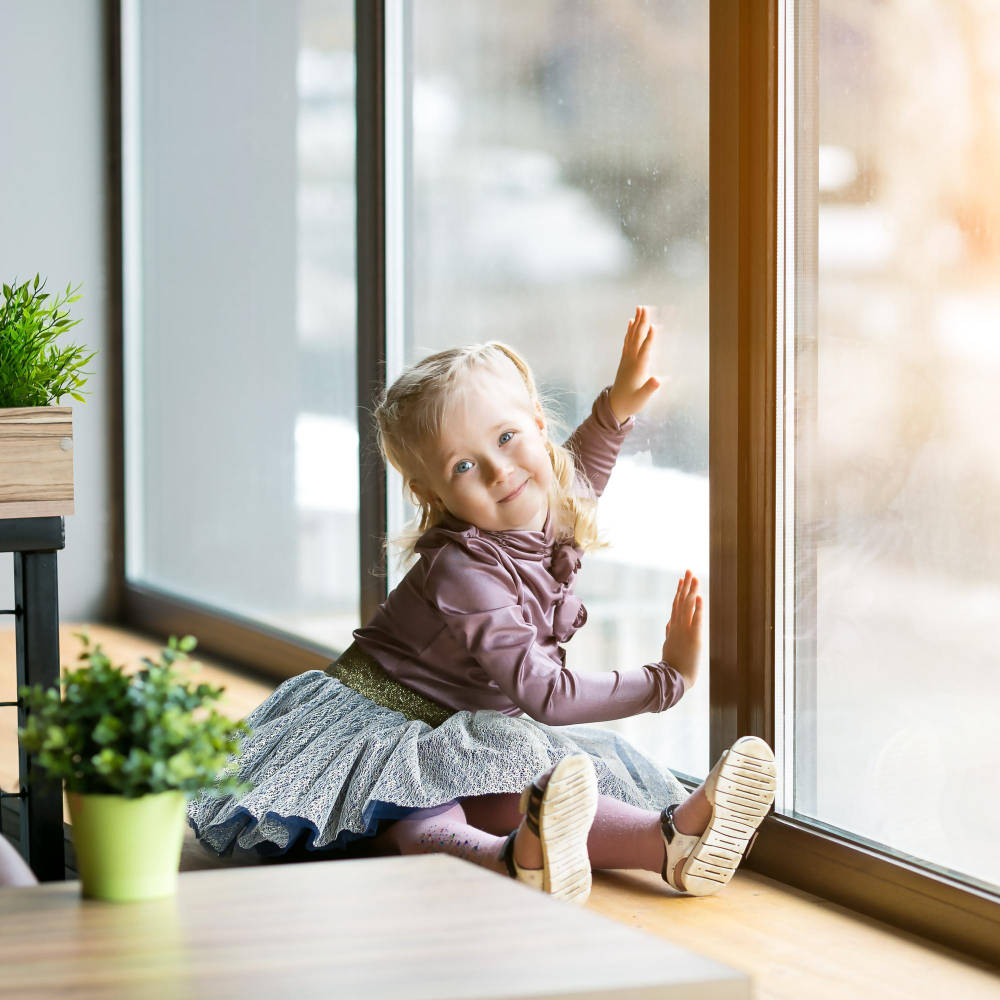 Porträt eines niedlichen lächelnden Mädchens, das zu Hause am Fenster sitzt